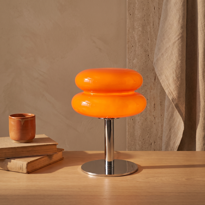 Bellona glass table lamp lit on a white oak desk beside books and a ceramic cup