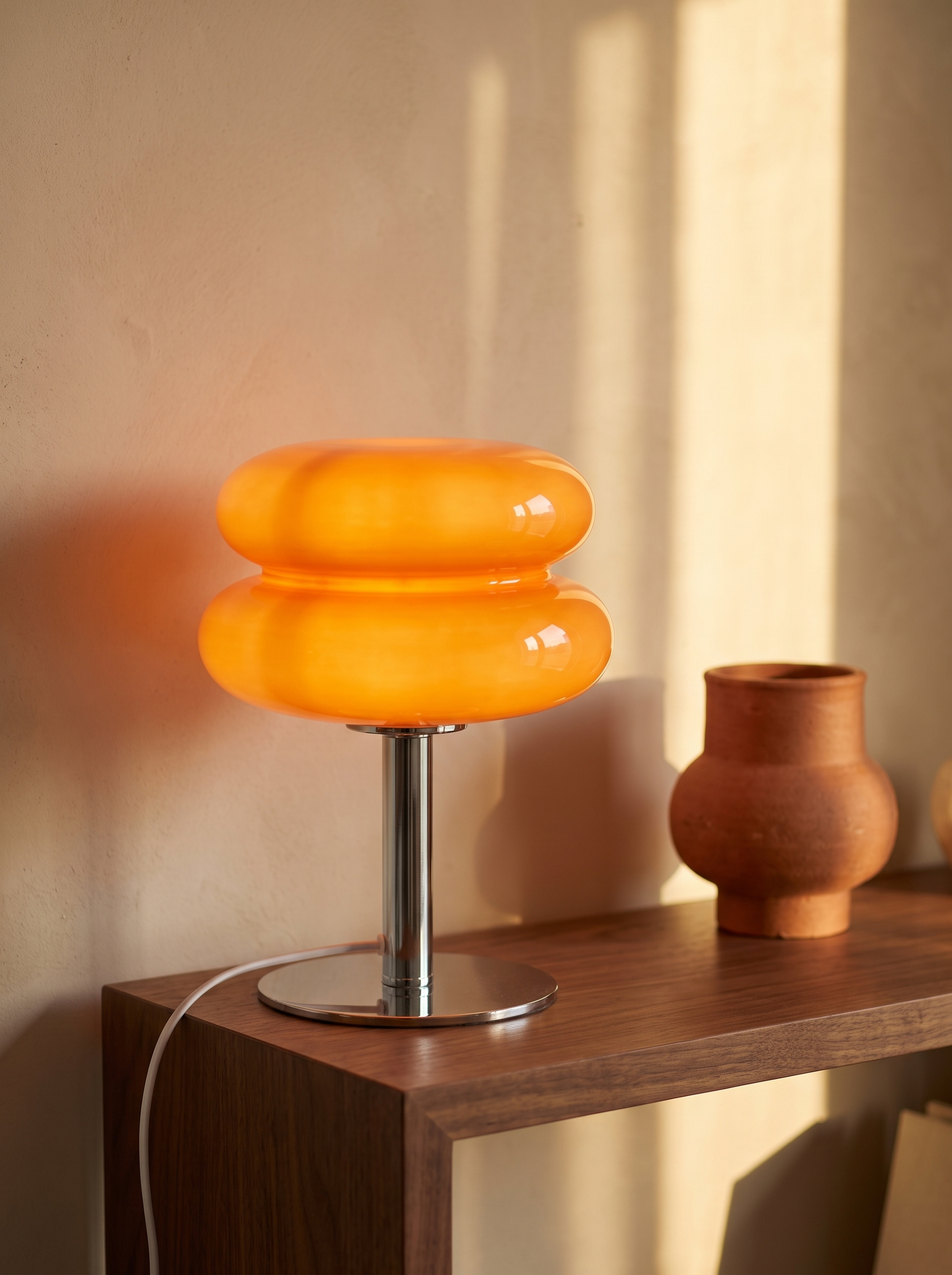 Bellona table lamp lit on a walnut shelf with its plug in cord running behind