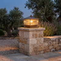 Rame copper pillar lantern lit at dusk on a dry stone gate pillar with olive trees behind